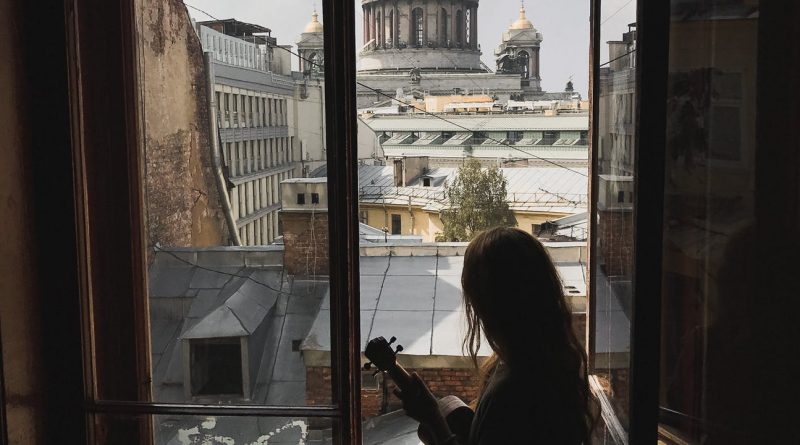 silhouette of a woman holding a ukulele sitting by the window looking at the city